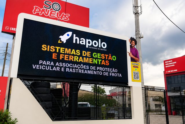 Painel de LED da BG Mídia na rua, exibindo o anúncio de um cliente, com a fachada de uma loja ao fundo.