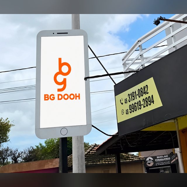 Painel de LED vertical montado em poste na Rua Aldo Hulse, no centro de Tubarão, ao lado da fachada de uma loja.